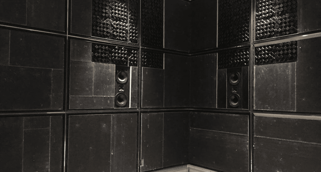 Dark, CinemaTech's high-performance acoustic paneling (ARS) setup with sound-absorbing materials and embedded speakers, creating an optimized audio environment. The panels are arranged in a grid pattern on the walls, featuring sections of textured diffusers and absorptive surfaces to enhance sound quality. The space is designed for superior acoustics, likely intended for a home theater or professional sound studio, emphasizing functionality and sound clarity.